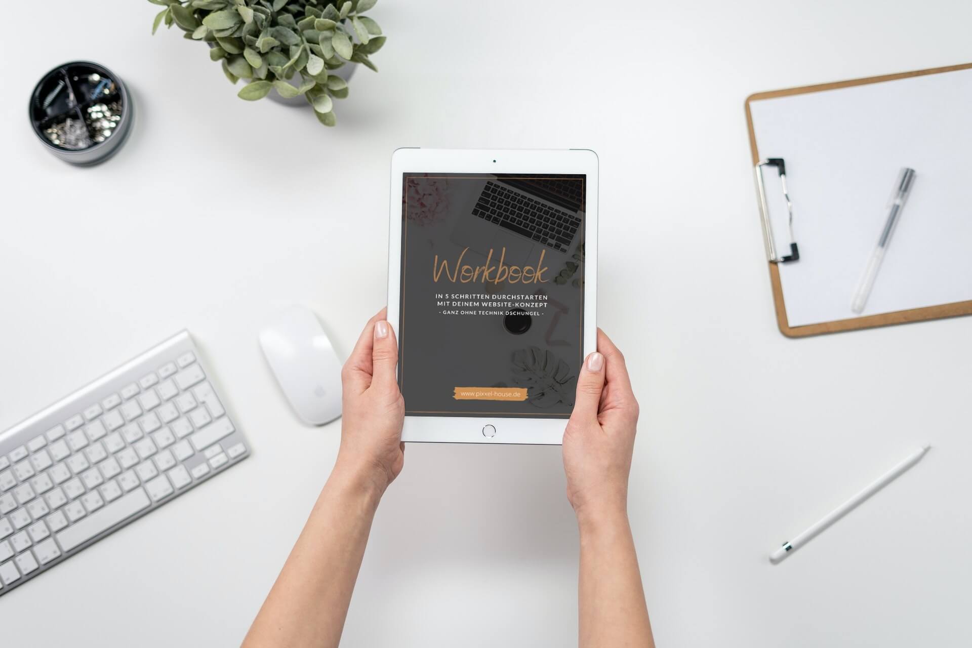 Eine Person hält ein Tablet mit dem Wort „Werkboek“ über einem eleganten Schreibtisch mit einer Pflanze, Tastatur, Maus, Bleistift und Klemmbrett. Die Umgebung ist hell und minimalistisch und ergänzt perfekt die Ästhetik modernen Webdesigns.