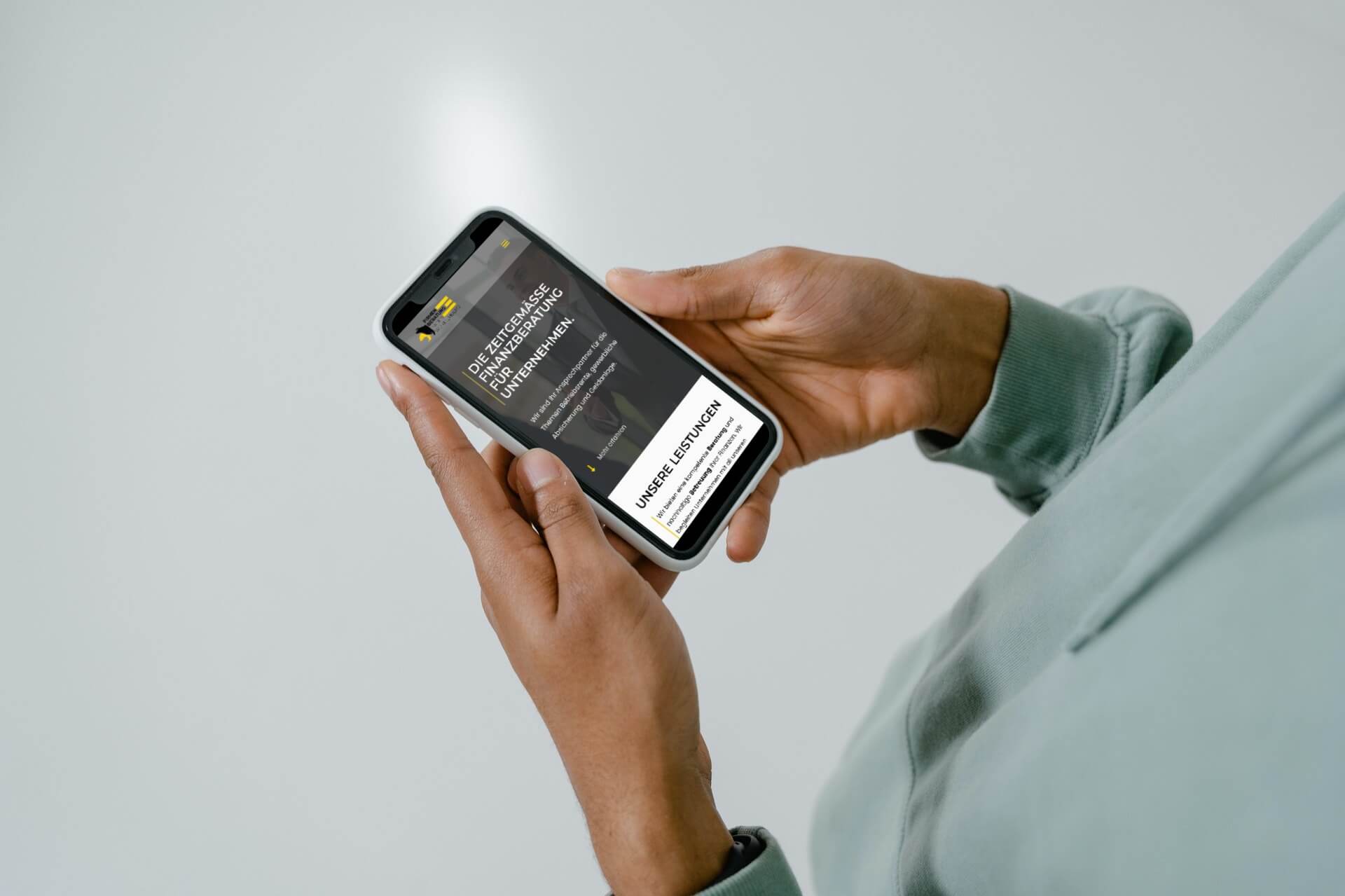 Eine Person hält ein Smartphone in der Hand und liest einen digitalen Newsletter mit dem Titel „BFCM-Strategien zum Ausprobieren: Erstellen von Preisen, Paketen und anderen Angeboten“. Sie trägt einen hellgrünen Kapuzenpullover vor einem neutralen Hintergrund und vertieft sich in die neuesten Tipps zur Suchmaschinenoptimierung und zum WordPress-Webdesign.